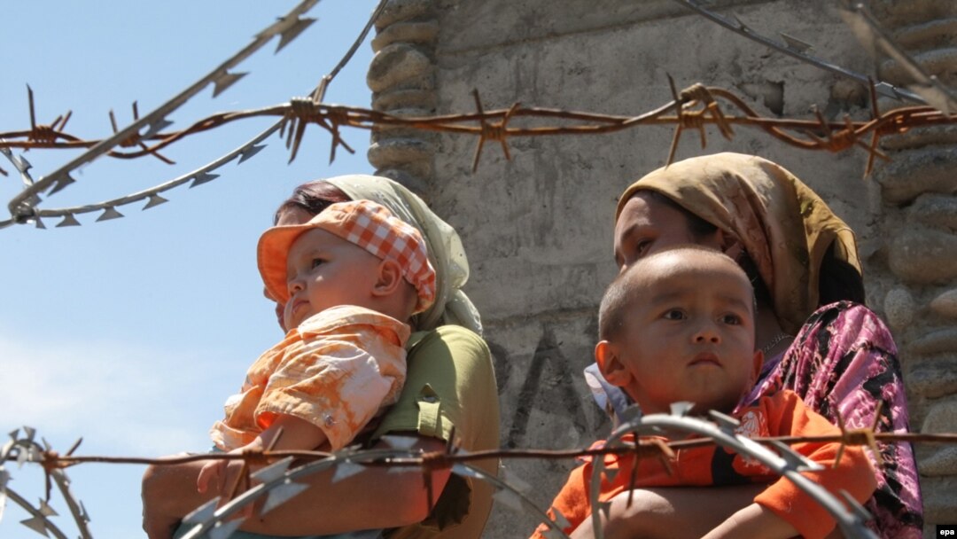 Ethnic Uzbek refugees walk behind a barbed wire fence as they queue to return to Kyrgyzstan at the border crossing near the city of Osh 
