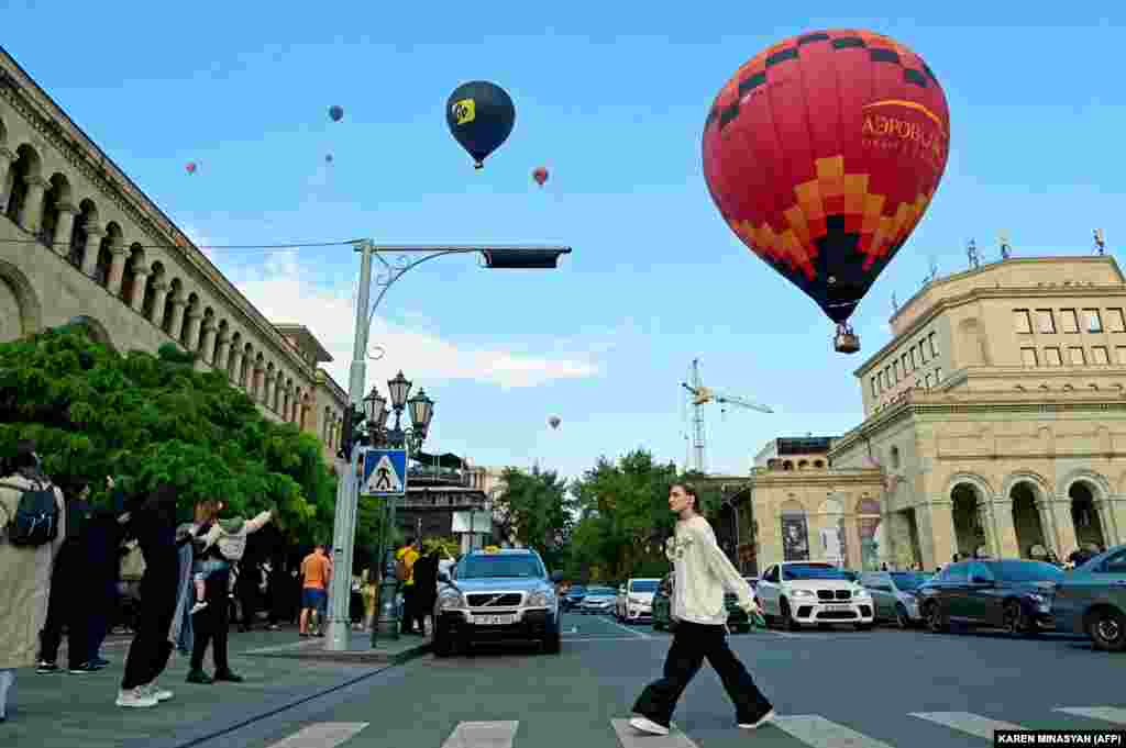 Këmbësorët duke kaluar rrugën ndërsa balonat me ajër të nxehtë fluturojnë mbi kryeqytetin armen gjatë festivalit vjetor të balonave, në Jerevan më 15 tetor.