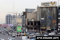 Аўтамабілі праяжджаюць міма спаленага падчас беспарадкаў будынка ў Тэгеране, 19 студзеня 2026