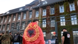 Një protestues i mbështjellë me flamur të Ushtrisë Çlirimtare të Kosovës, qëndron pranë selisë së Dhomave të Specializuara të Kosovës në Hagë, teksa gjykatësi shqipton aktgjykimin ndaj ish-krerëve të UÇK-së, në Hagë, Holandë, 16 shtator 2026.