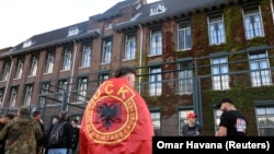 Një protestues i mbështjellë me flamur të Ushtrisë Çlirimtare të Kosovës, qëndron pranë selisë së Dhomave të Specializuara të Kosovës në Hagë, teksa gjykatësi shqipton aktgjykimin ndaj ish-krerëve të UÇK-së, në Hagë, Holandë, 16 shtator 2026.