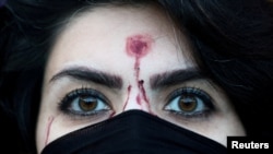 A woman with a mock-up of a gunshot bullet wound on her forehead looks on during a rally in support of nationwide protests in Iran in Rome, Italy, on January 13