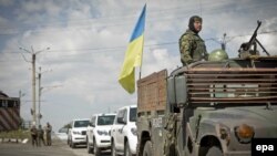 A Ukrainian soldier watches from an armored vehicle with a Ukrainian flag in front of OSCE vehicles at a checkpoint in the village of Debaltseve, in eastern Ukraine, on July 31.