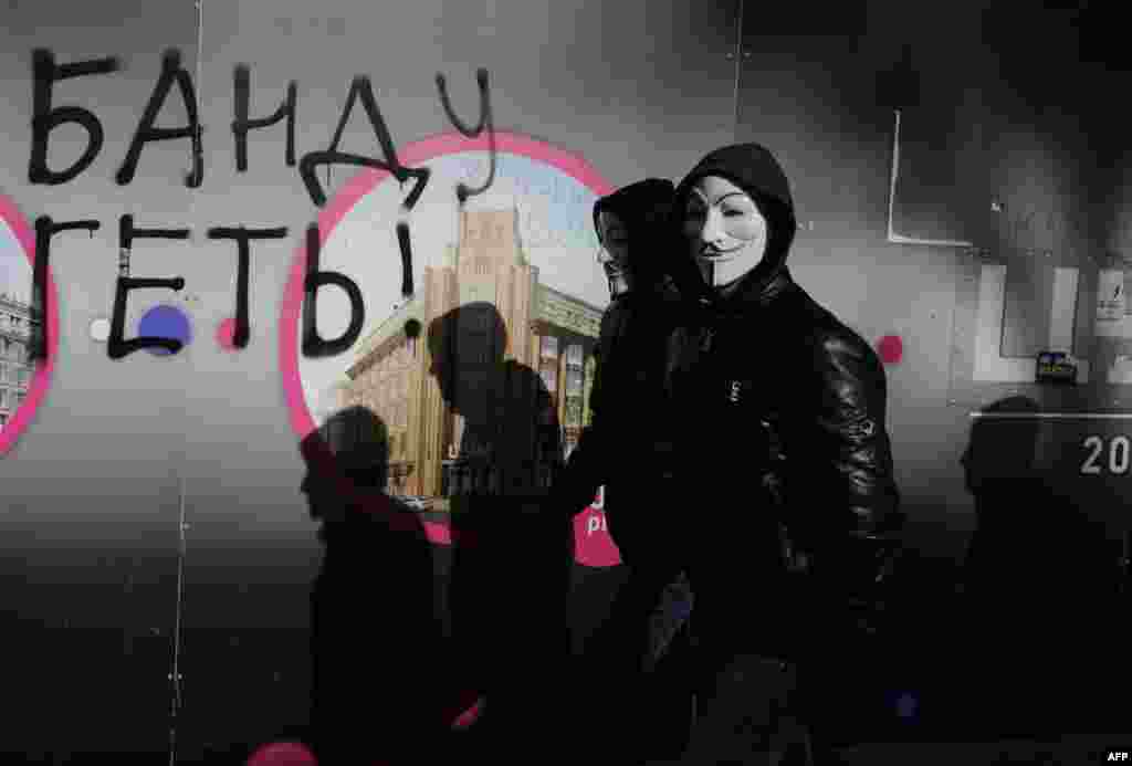 Protesters wearing "V for Vendetta" masks walk past graffiti reading "Down with the gang!" after an antigovernment protest in the center of Kyiv on February 6. (AFP/Aleksandr Chekmenev)