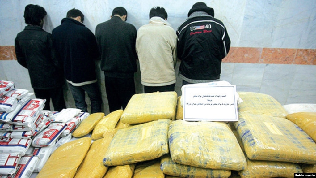 A pile of drugs is displayed in front of a group of suspected drug traffickers arrested in Iran.