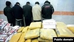 A pile of drugs is displayed in front of a group of suspected drug traffickers arrested in Iran.