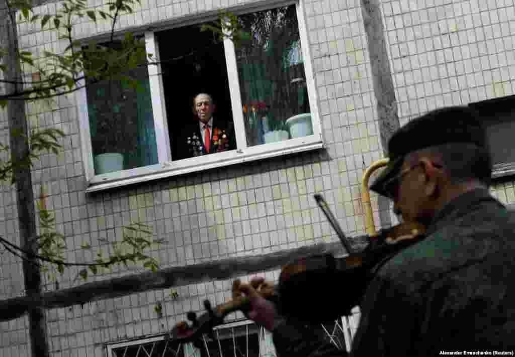 A 96-year-old World War II veteran watches from his apartment window as a band plays in his honor during Victory Day celebrations on May 9 in Donetsk, Ukraine.