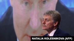 Пресс-секретарь Кремля Дмитрий Песков на фоне экрана с изображением президента России Владимира Путина