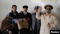 Ресейде жүрген шетелдік жұмысшылар Ленин мен Сталин болып киініп алған адамдардың қасында суретке түсіп тұр. Мәскеу, 6 қазан 2011 жыл. 