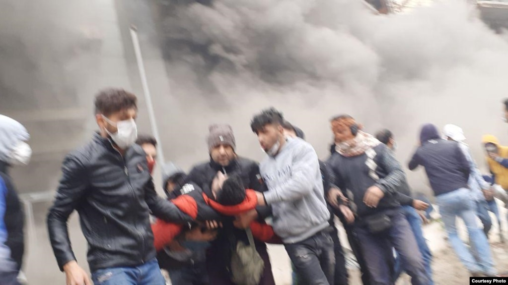 Young protesters carrying away a comrade during fierce protests in Shiraz, Iran. November 2019