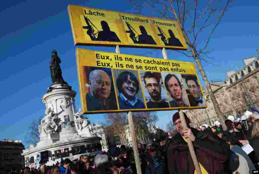 A man holds a sign bearing the portraits of slain Charlie Hebdo staffers.