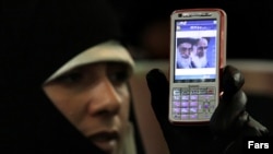 Ирандық әйелдің қолындағы мобильдік телефонда Иранның ең жоғарғы дінбасы – аятолла Хаменеи мен Иран Ислам Республикасының негізін қалаған аятолла Хомейни бейнеленген. Теһрандағы оппозиция наразылығы. Желтоқсан, 2009 жыл.