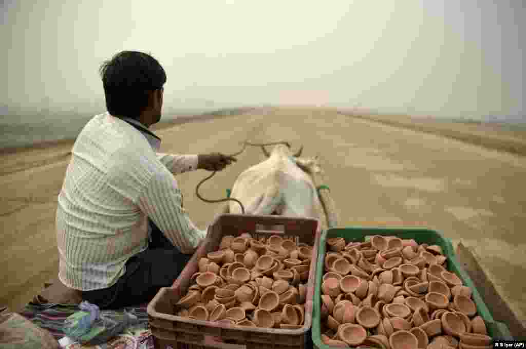 A Indian man selling traditional earthen lamps rides a bullock cart on an unfinished road on a foggy day in Greater Noida, near New Delhi. (AP/R.S. Lyer)