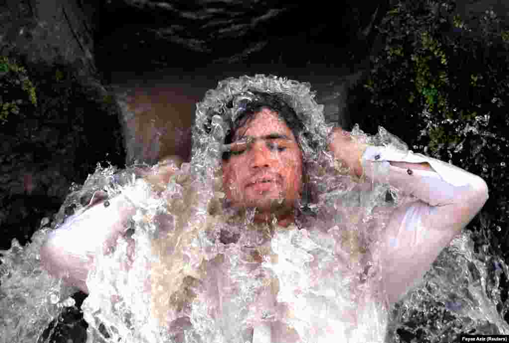 A man cools off under a water pipe from a canal in hot and sunny weather on the outskirts of Peshawar, Pakistan. (Reuters/Fayaz Aziz)