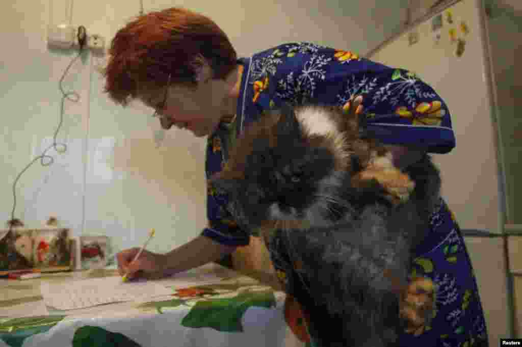 A woman holds her cat as she signs a form before casting her vote into a portable ballot box inside her house in the village of Slobodschina.