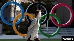 Женщина в маске проходит в Токио рядом с инсталляцией в форме олимпийских колец.