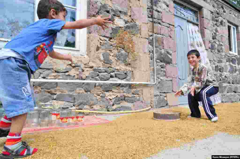 Дети играют с семенами выложенного для просушки ячменя, Гегаркуниксая область Армении