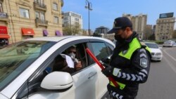 Азербайджанский полицейский в маске проверяет документы водителя остановленной им машины.