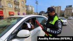 Азербайджанский полицейский в маске проверяет документы водителя остановленного автомобиля в Баку.