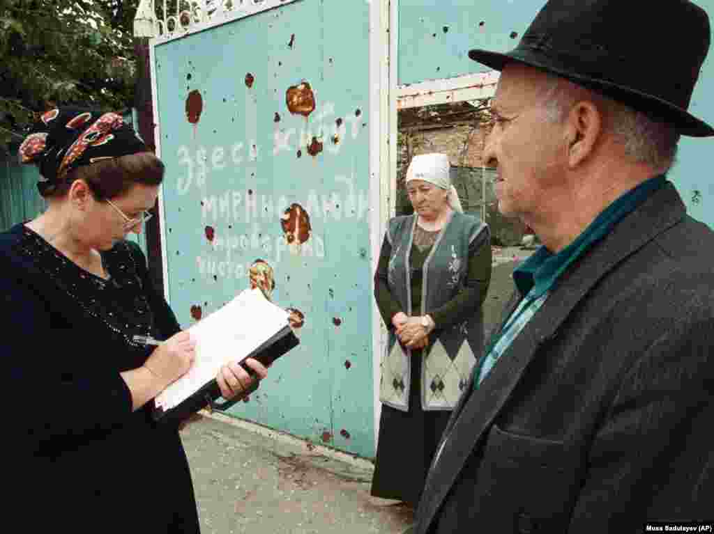 Two Chechen residents answer a census worker&rsquo;s question outside their battle-scarred gate in 2002. Writing on the gate, which probably dates to the Chechen wars of the 1990s, says, &ldquo;Peaceful people live here. Checked to be safe.&rdquo;