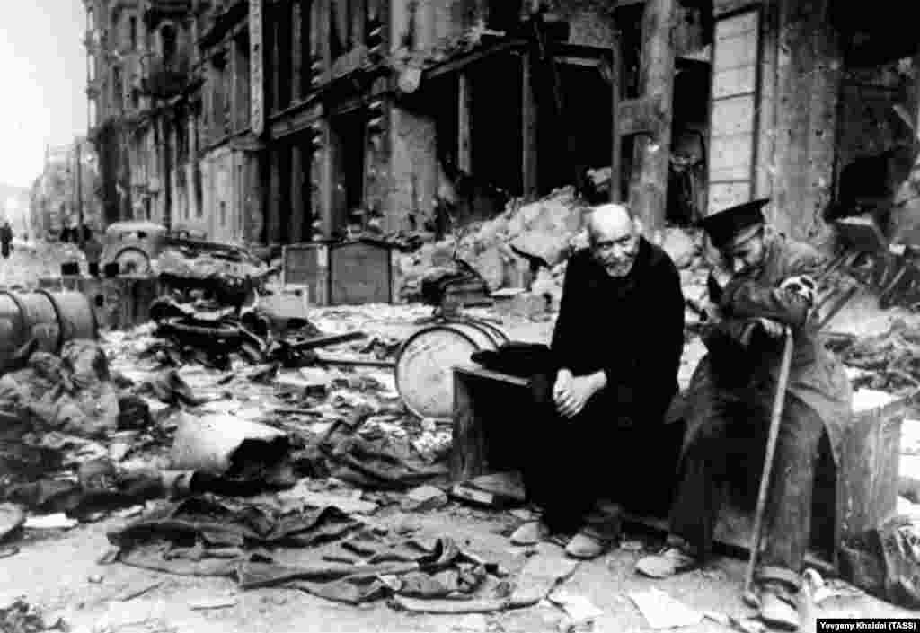 Сляп човек (вдясно) и негов приятел седят в останките на улица в Берлин скоро след края на войната. Войната в Европа свършва през май 1945 г., след като Съветската армия и съюзническите войски нахлуват в центъра на Берлин, превземат бункера на Адолф Хитлер и закачат комунистически знамена на знакови места в германската столица.