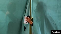 People are seen behind the curtain of a voting booth in Minsk during parliamentary elections on September 23.