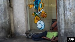 یک بی‌خانمان در شهر ریوی برزیل زیر تصویری از نماد جام جهانی ۲۰۱۴، خوابیده است