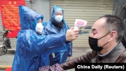 A worker takes body temperature measurement of a man at the entrance to a residential compound following an outbreak of the new coronavirus in Wuhan, Hubei province, February 1, 2020