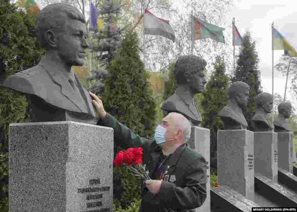 A Ukrainian man wearing a face mask and holding a bunch of red flowers touches one of the busts of a monument honoring those who died in cleanup efforts after the Chernobyl nuclear disaster, in Kyiv on the 34th anniversary of the tragedy on April 26. (epa-EFE/Sergey Dolzhenko)