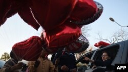 Сотрудник пакистанской полиции (справа) рядом с торговцами воздушными шарами в форме сердец. Исламабад, 13 февраля 2017 года.
