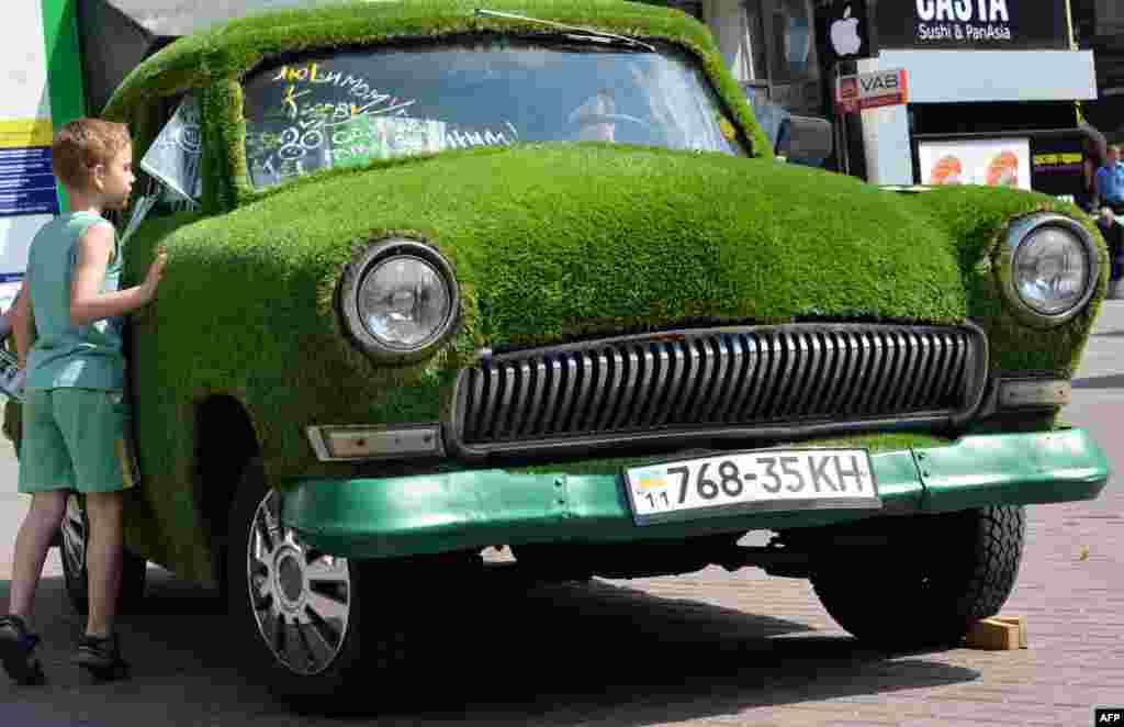 A Ukrainian boy looks at a GAZ-21 Volga car decorated with grass and parked in Kyiv. (AFP/Sergei Supinsky)