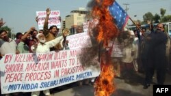 A Pakistani protester from United Citizen Action holds a burning U.S. flag as others shout anti-U.S. slogans during a protest against the killing of Taliban leader Hakimullah Mehsud, reportedly in a U.S. drone attack in Pakistani tribal region.