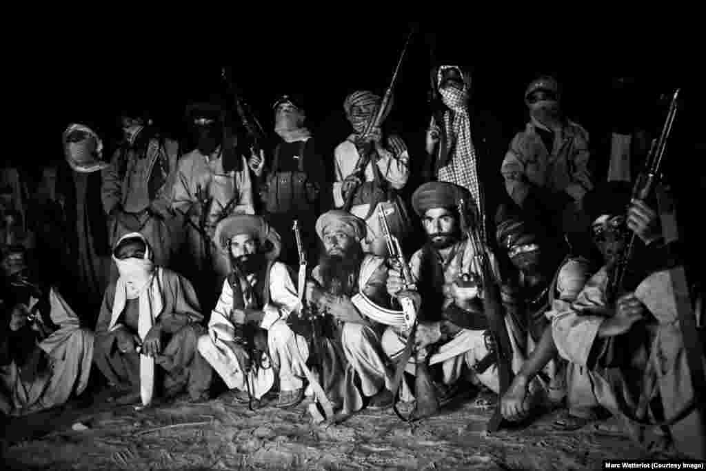 A group of fighters from the Baloch Liberation Army pose with their weapons around the campfire.