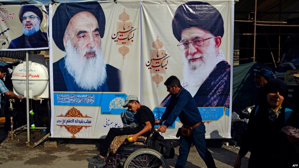 Shiite Muslim pilgrims in Iraq walk in front of posters of (R to L) Iran's Supreme Leader Ayatollah Ali Khamenei, the spiritual leader of the Shiite community Grand Ayatollah Ali Sistani, and the leader of Lebanon's Hezbollah movement Hasan Nasrallah. October 12, 2019.