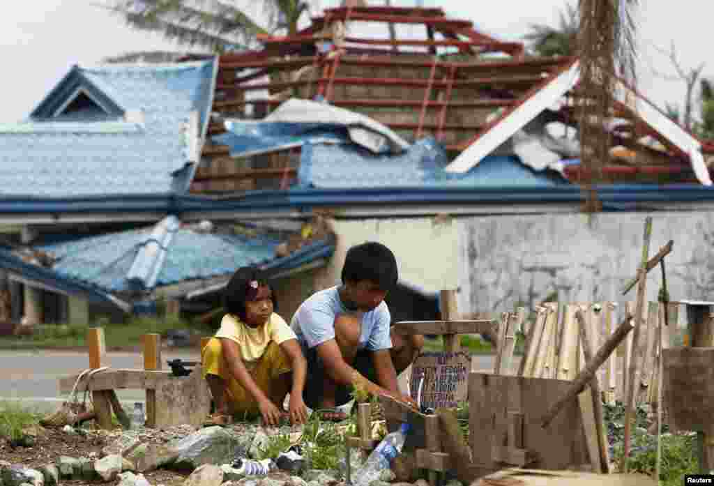 Romualdo Redona and his younger sister Angel offer prayers and candles at the grave of their siblings who were killed by supertyphoon Haiyan a month ago and buried in a vacant lot along a main road in Tanuan, in the Philippines' Leyte province. (Reuters/Romeo Ranoco)