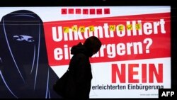 People walk by a campaign poster urging Switzerland to vote no in a proposed referendum on granting citizenship to the grandchildren of immigrants, which sparked anti-Muslim sentiment in some quarters. 