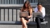 Young women work on laptops while waiting for a bus in Moscow.