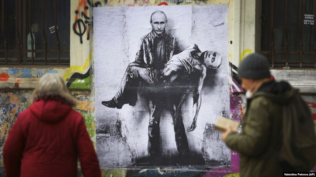 Люди проходять повз мурал болгарського художника Станіслава Бєловського, на якому президент Росії Володимир Путін тримає своє тіло, у час масштабного вторгнення Росії в Україну. Софія, Болгарія, 28 березня 2022 року