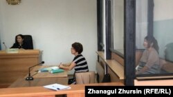 Акмарал Алмагамбетова (справа, за стеклянной перегородкой) в зале суде, где ей предъявлены обвинения в «пропаганде терроризма» и «возбуждении розни». Актобе, 22 июля 2019 года.