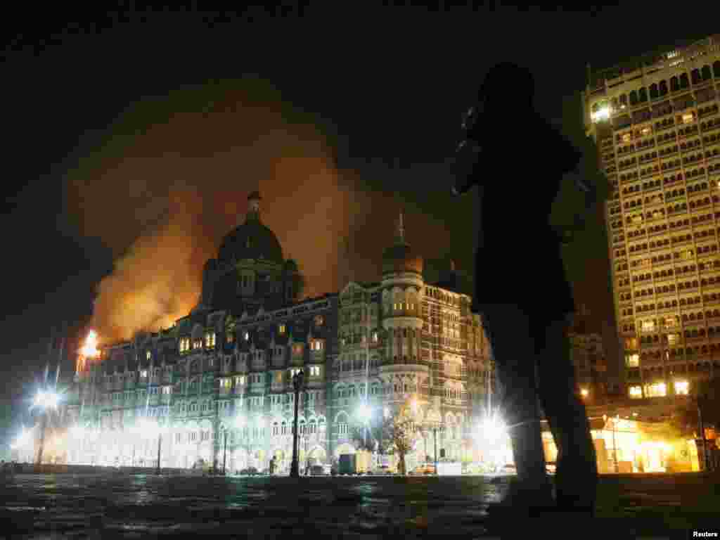 A reporter talks on her phone as smoke is seen coming from Taj Hotel in Mumbai November 27, 2008. Large plumes of smoke were seen rising from the top of the landmark Taj Hotel in Mumbai on Thursday and heavy firing could be heard, a Reuters witness said. Local TV reported that unknown assailants had earlier attacked the hotel, taking hostages, including Western tourists. REUTERS/Arko Datta 