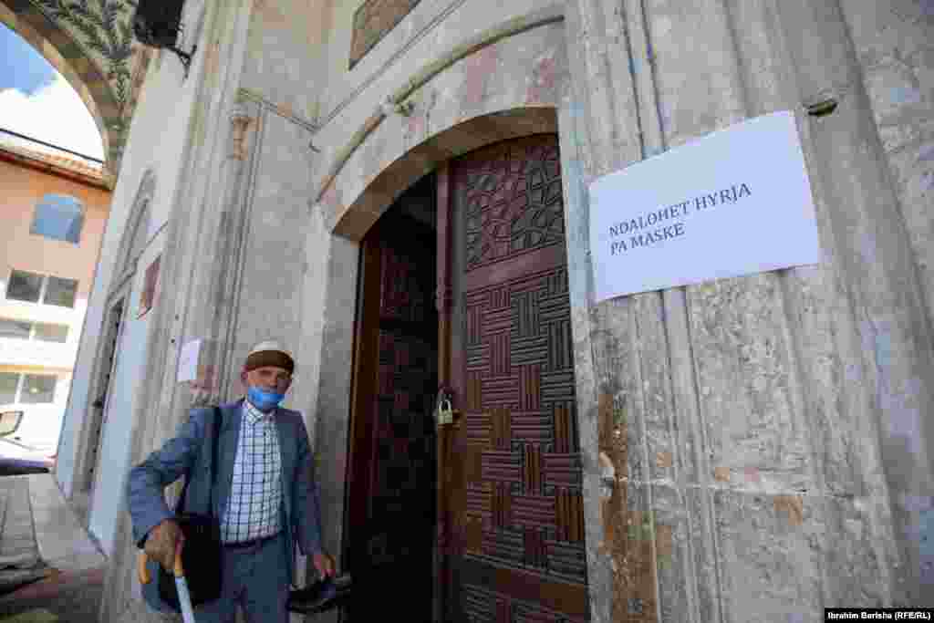 An old man enters a mosque in Pristina, Kosovo, while taking note of a sign that forbids entry to those not wearing face masks.