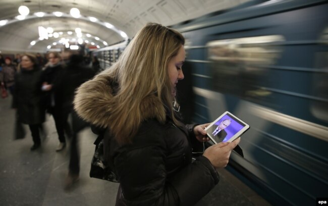 A young woman watches Vladimir Putin's annual press conference on a mobile device in a Moscow subway station. (file photo)