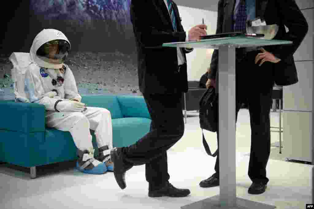 A man in a spacesuit is seen sitting on a couch behind two businessmen at the Wittenstein booth at the Hannover industrial fair in Hannover, Germany. The fair presents a cross-section of key industrial technologies. (AFP/Odd Andersen)