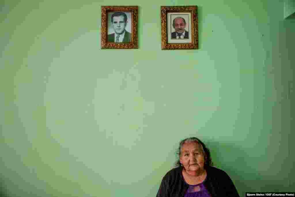 A Romany grandmother, originally from the city of Liberec in the Czech Republic, sits under portraits of her deceased son and husband.