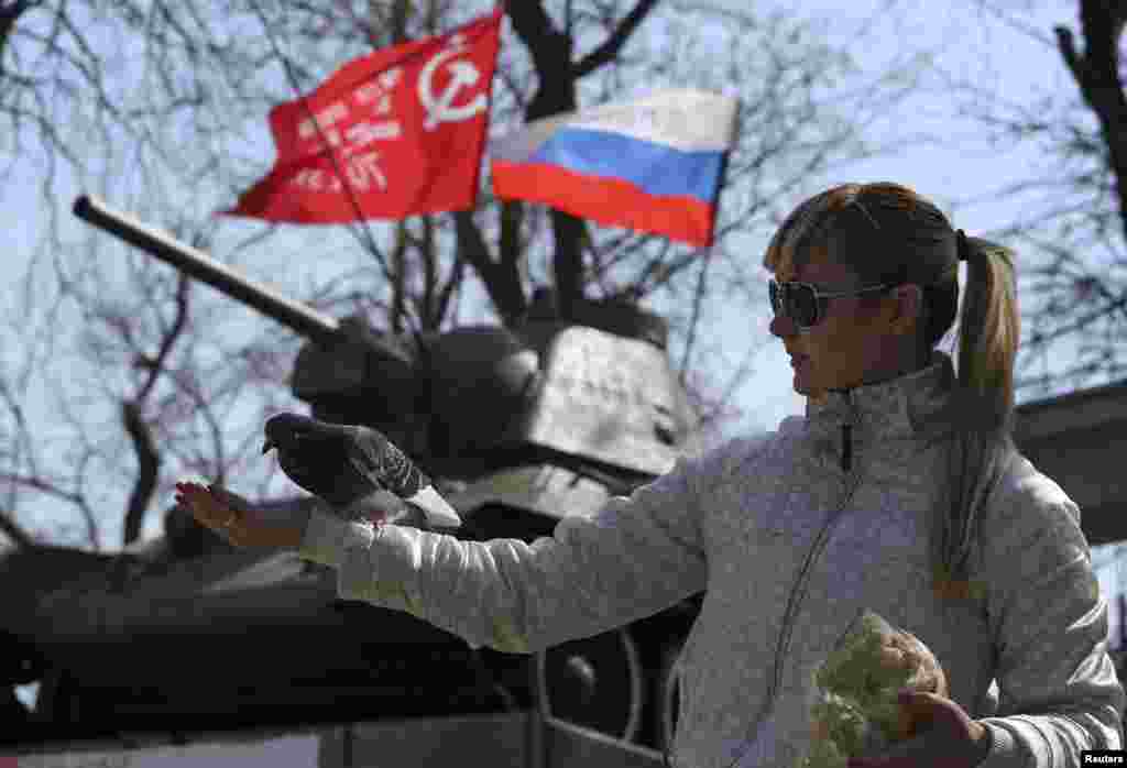 Ukraine - A woman feeds a pigeon near a monument displaying a Soviet-era tank on the eve of a referendum in Simferopol, March 15, 2014.