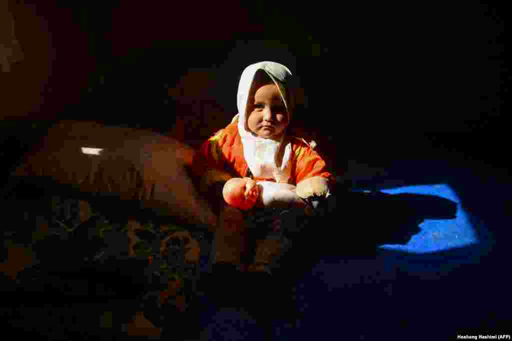 An internally displaced Afghan girl looks on as she holds a doll inside her temporary home at a refugee camp on the outskirts of Herat. (AFP/Hoshang Hashimi)