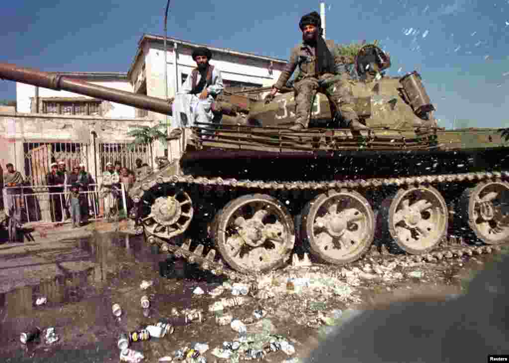 Taliban enforcers pop beer cans under a Soviet tank in Kabul. Alcohol was also strictly forbidden. Punishments for offenders against the Taliban's Shari'a edicts were often gruesome, and public.