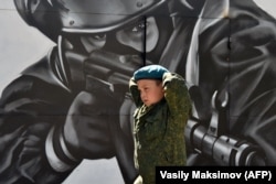 Egy fiú terepszínű ruhában sétál a különleges erők katonáját ábrázoló falfestmény előtt a Nemzeti Gárda által szervezett katonai jellegű versenyen, egy Moszkva melletti gyakorlótéren