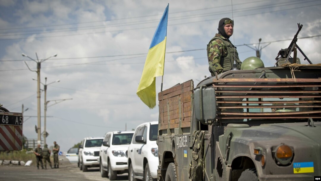 A Ukrainian soldier watches from an armored vehicle with a Ukrainian flag in front of OSCE vehicles at a checkpoint in the village of Debaltseve, in eastern Ukraine, on July 31.