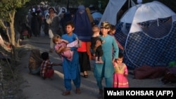 Internally displaced Afghans who fled from Kunduz, Takhar, and Baghlan provinces due to battles between the Taliban and Afghan security forces walk past temporary tents at the Sara-e Shamali camp in Kabul on August 11.